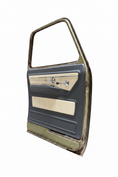 Load image into Gallery viewer, A used vintage car door panel with a dark gray vinyl outer frame, beige woodgrain trim, and chrome door handle and lock hardware, photographed inside a garage.

